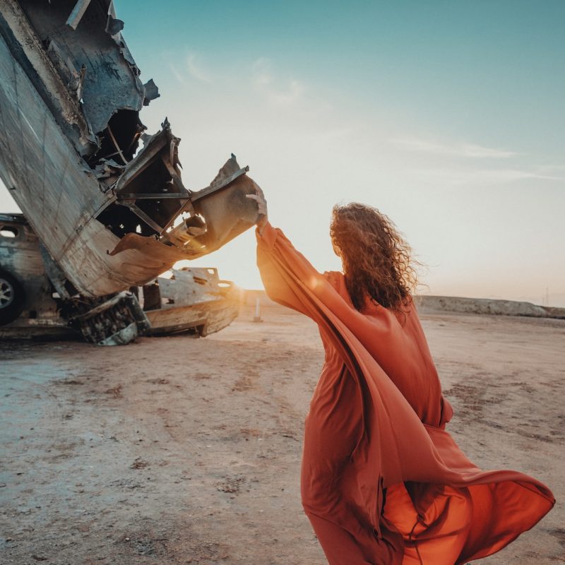 a woman in an orange dress standing in front of a wrecked airplane